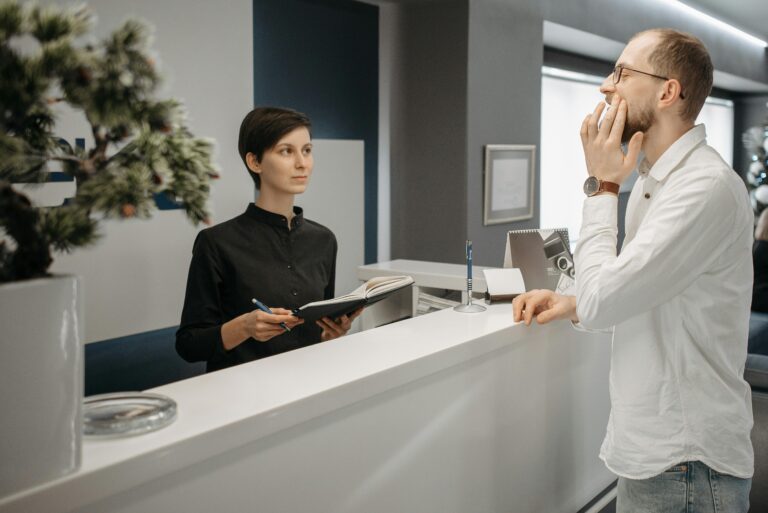 Man holding his jaw in pain while standing at a dental clinic reception, arriving late for treatment.