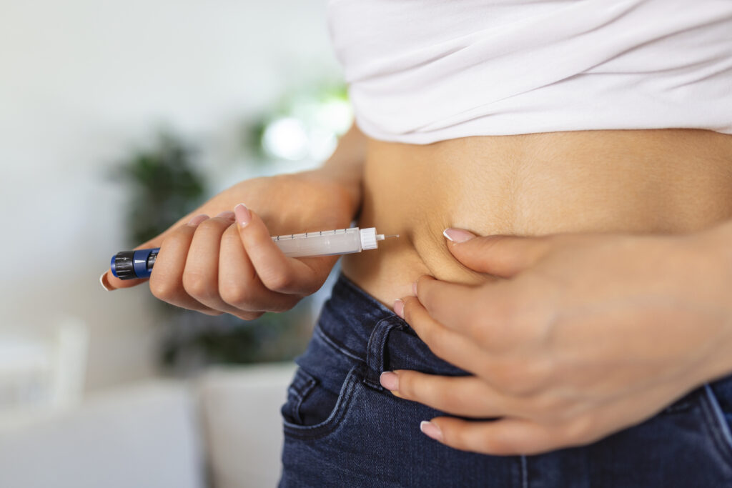 A woman self-administering a Wegovy injection in her abdomen as part of her weight-loss regimen, highlighting the growing link between Wegovy & oral health concerns.