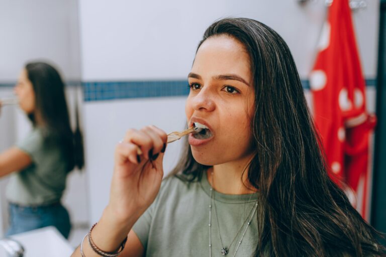 An Indian woman brushing her teeth in front of a bathroom mirror, emphasizing the importance of daily oral hygiene in managing the effects of Wegovy & oral health.
